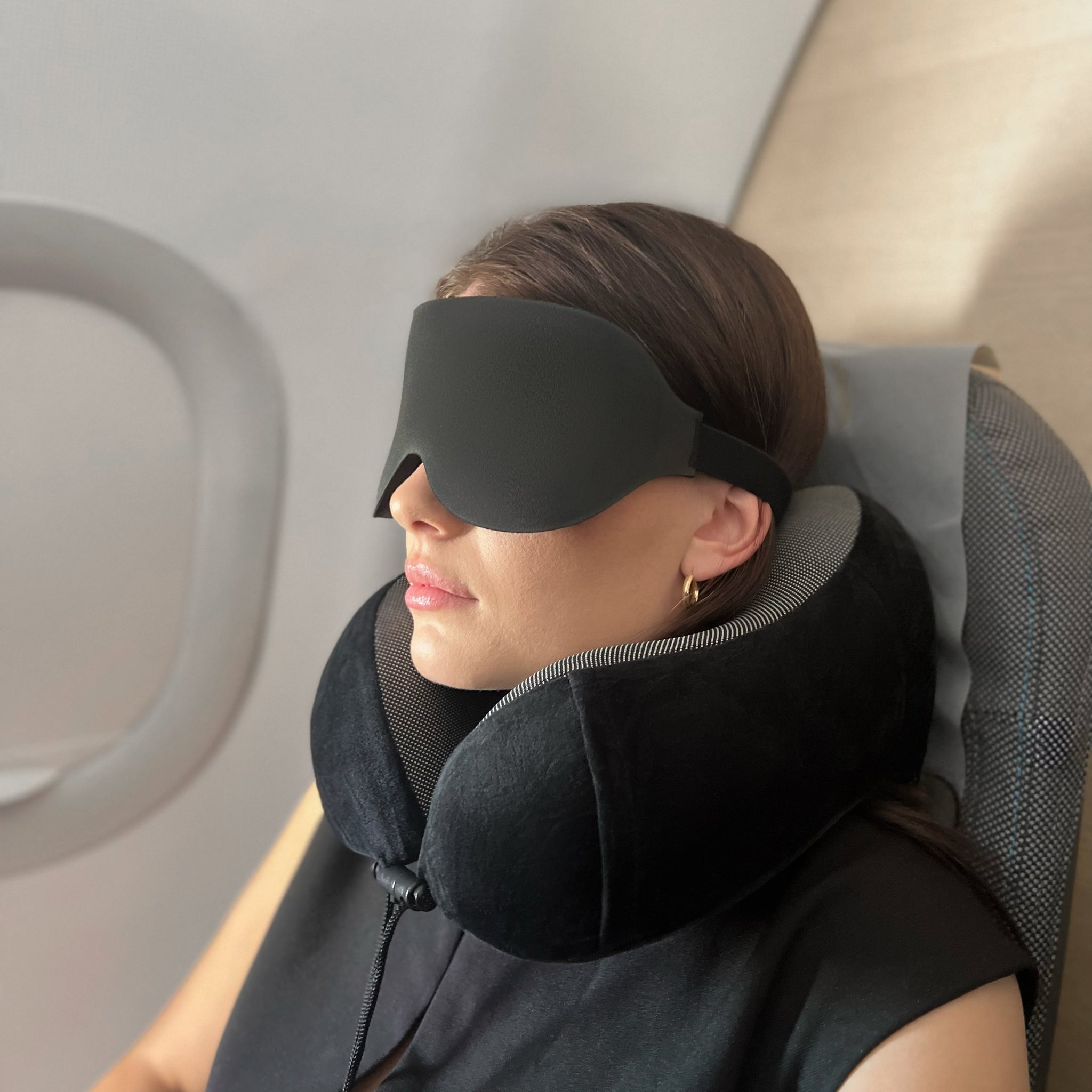 Person som hviler i flysete med svart sovemaske og ergonomisk nakkepute fra NORZEN reisesett